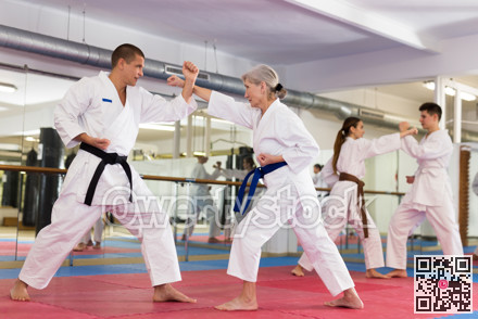Elderly woman in kimono practicing martial arts techniques with trainer