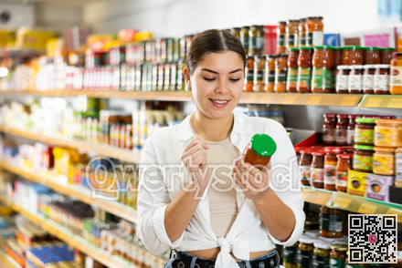 Young woman choosing preserved vegetables for herself in supermarket