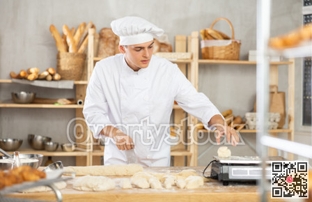 Young male baker cutting and weighing dough on scales in bakehouse