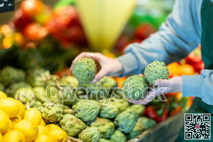 Close-up of salesperson hand put ripe artichokes on grocery supermarket display
