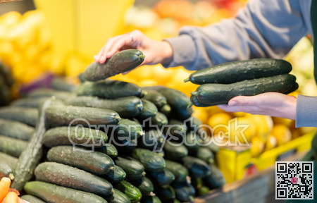 Closeup of shopper hand selecting ripe cucumbers from supermarket shelves