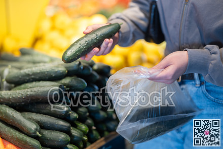 Close-up of female seller's hands putting cucumbers into plastic bag