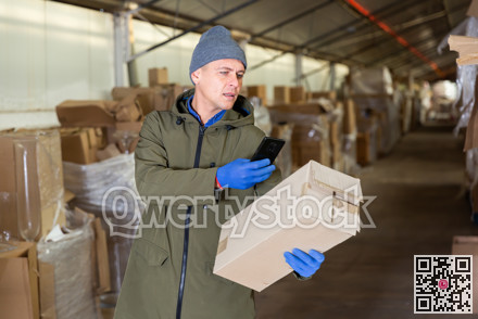 Warehouse worker photographing cardboard box with his phone