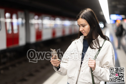 Girl is standing on metro platform station, scrolling through mobile phone