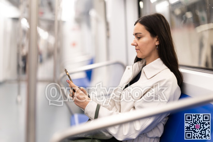 Woman sits in subway wagon and prints message on her mobile phone. Uses online navigator to use public transport