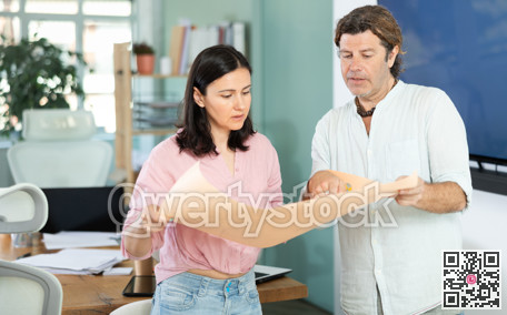 Middle-aged man and woman discussing construction plan standing in office