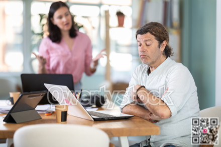 Woman scolding sad colleague sitting at laptop in office