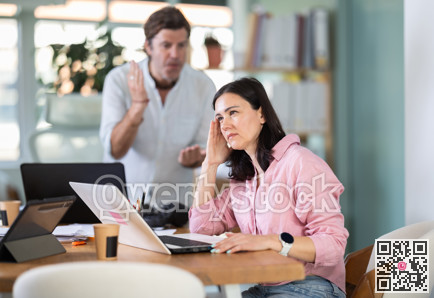 Adult man scolding adult female colleague working on laptop