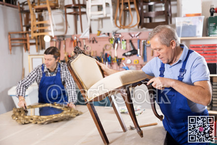 To replace upholstery, restorer removes old cloth seat covering from antique wooden chair.