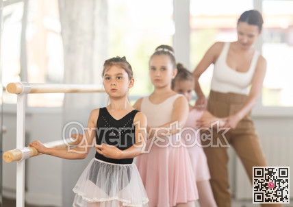 Girls in ballet class perform first position with correction of female mentor