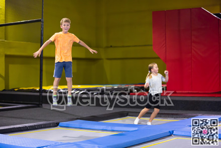 Joyful school-age boy in casual clothes bouncing on trampolines indoors in leisure sport center for kids
