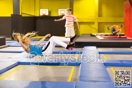 Joyful teen girl in sport clothes bouncing on trampolines indoors in leisure sport center for kids