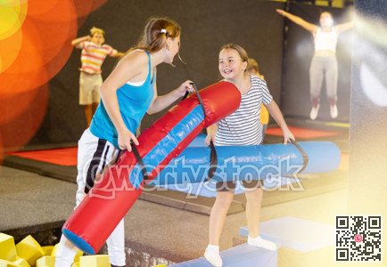 Children girls having fun and playing with inflatable sticks on the trampoline arena while spending time together on weekend