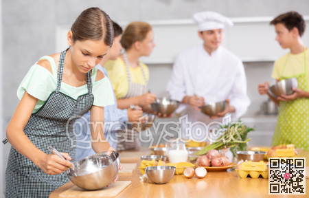 During cooking classes, girl carefully mixes ingredients in bowl with whisk.