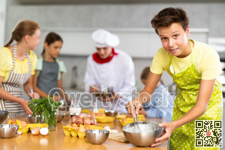 During cooking classes, teen boy carefully mixes ingredients in bowl with whisk