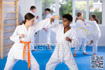 Teen girl karateka honing punches in kumite with african boy