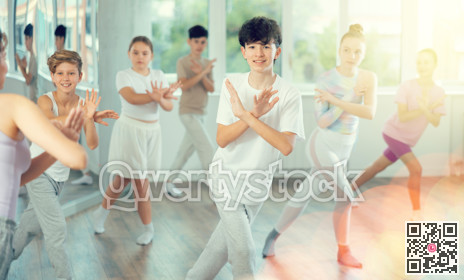 Male boy student repeats movements of unrecognizable teacher during group modern dance class.