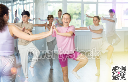 Female girl student repeats movements of unrecognizable teacher during group modern dance class.