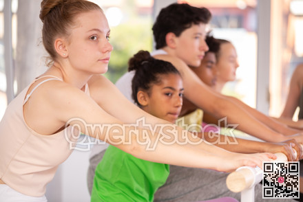 Teenage girl doing leg stretching exercise holding by ballet barre during dance courses