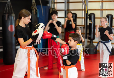 Teenage girl in boxing mitts trains with boy in boxing gloves