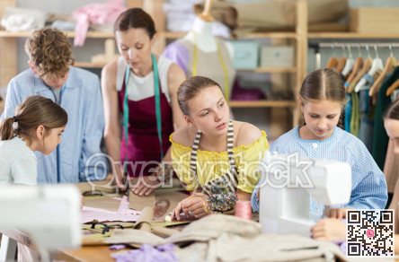 Teen girl watching peer sewing at machine during class