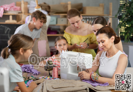 Woman teacher sews product surrounded by students