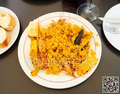 Paella made of rice, chicken and different seafood served in white plate with table appointments