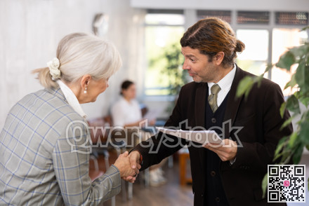 Adult man and elderly woman shaking hands in office