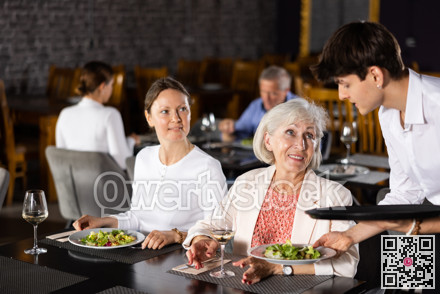 Young waiter serving dishes to female guests in restaurant