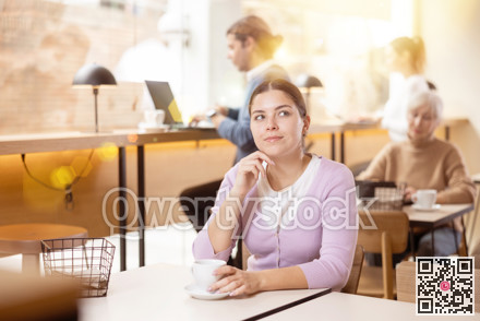 Dreamy young girl drinking coffee in cozy cafe