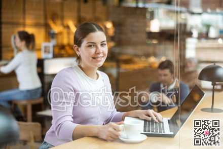 Young millennial woman sitting at table, using laptop and enjoing cup of tea in coffee house. Modern female lifestyle concept