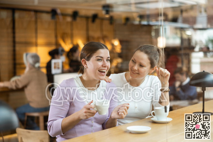 Two cheerful women chatting and drinking coffee at the bar counter of cafe