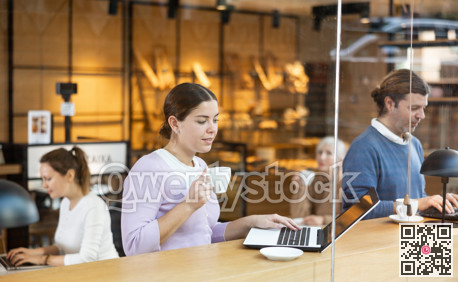 Smiling woman using laptop and drinking coffee in modern cafe