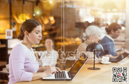Young female freelancer sitting in cafe with cup of coffee and laptop