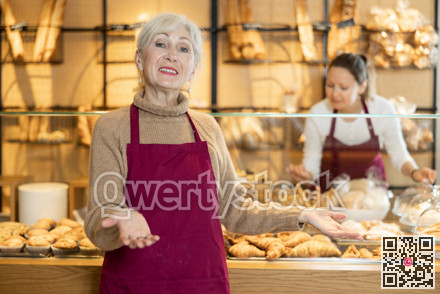 Cheerful mature female baker welcoming everyone into her bakery