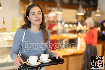 Girl visitor in self-service cafeteria carries tray with two cups of coffee.