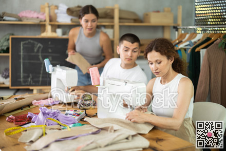 Multiethnic participants in coterie practice sewing, chatting, work textile and paper dress pattern