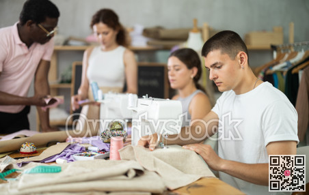 Engaged guy stitching fabric on machine in sewing class for adults