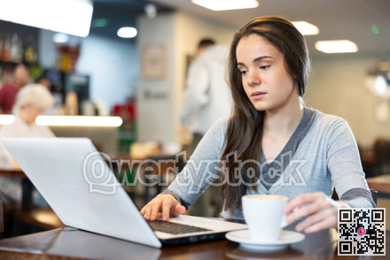 In cozy cafe hall, freelance young woman using laptop and drinks coffee.