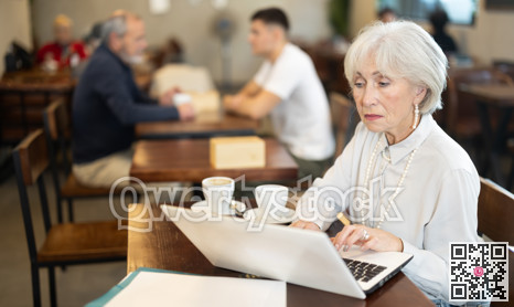 In cozy cafe hall, freelance senior woman using laptop and drinks coffee.