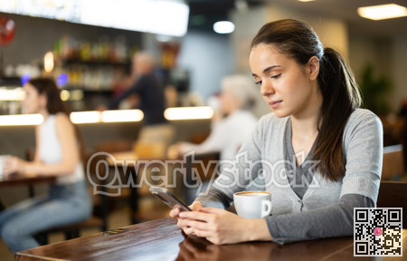 Girl in cafe drinks coffee and using mobile phone