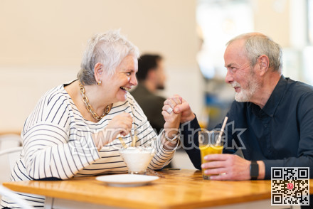 Elderly married couple are chatting happily with each other while sitting at table in a cafe and drinking juice and eat ice