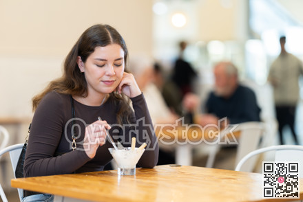 Food court girl visitor sits near table, eating ice cream in chain cafe shop