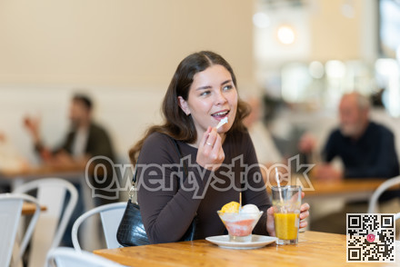 Food court girl visitor sits near table, eating ice cream in chain cafe shop