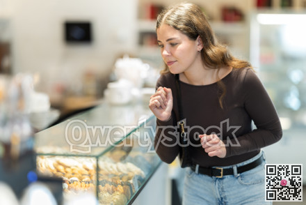 Young woman in casual clothes choosing sweet pastries at pastry shop display