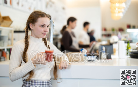 Teenage girl standing near the counter and drinking tomato juice