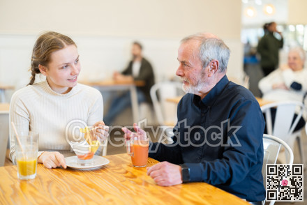 Grandfather and teenage girl sitting at table in cafe.
