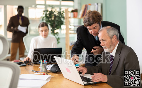 Middle aged man helping elderly employee with program on laptop
