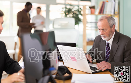 Mature man works online with a team of managers in company office.