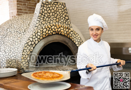 Portrait of young woman chef working in restaurant kitchen, getting ready pizza out of oven